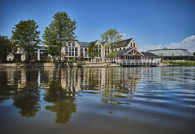 Große Bäume beschatten das moderne Gebäude am Wasser